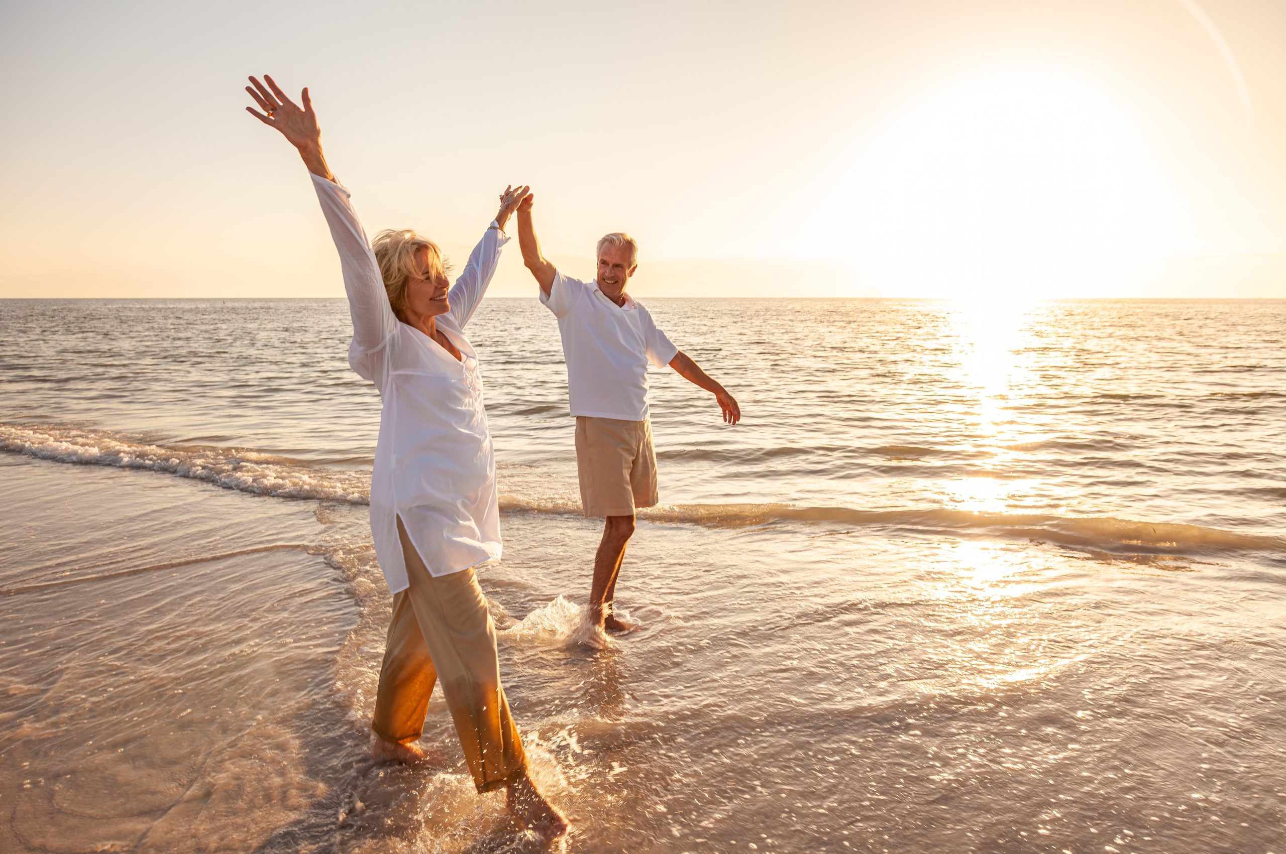 older couple walking on the beach with their hands raised